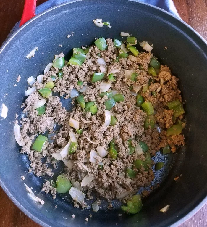 pot with ground beef, onions and chopped bell peppers inside.
