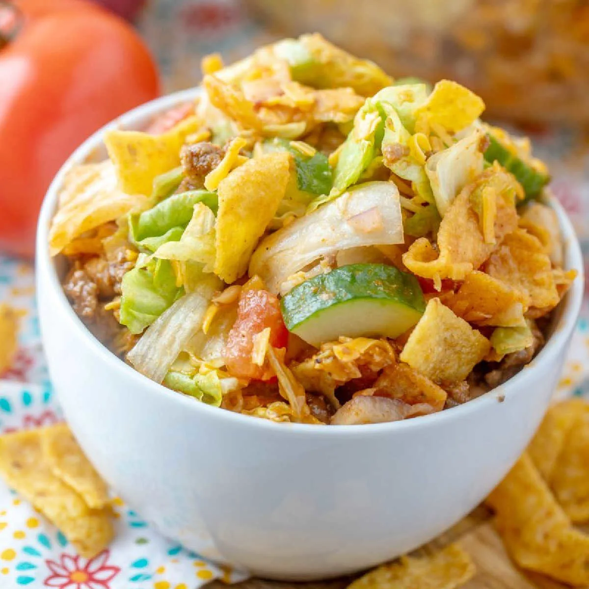 Close bowl of frito salad showing lettuce, cucumbers, cheese, taco meat and fritos all tossed in homemade catalina dressing.