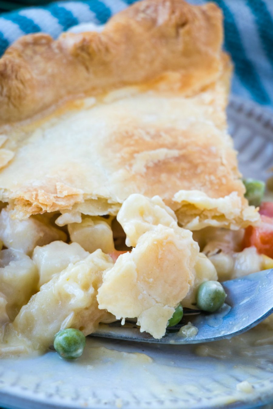 Fork getting a bite of creamy chicken pot pie showing veggies, potatoes, and chicken in the filling.
