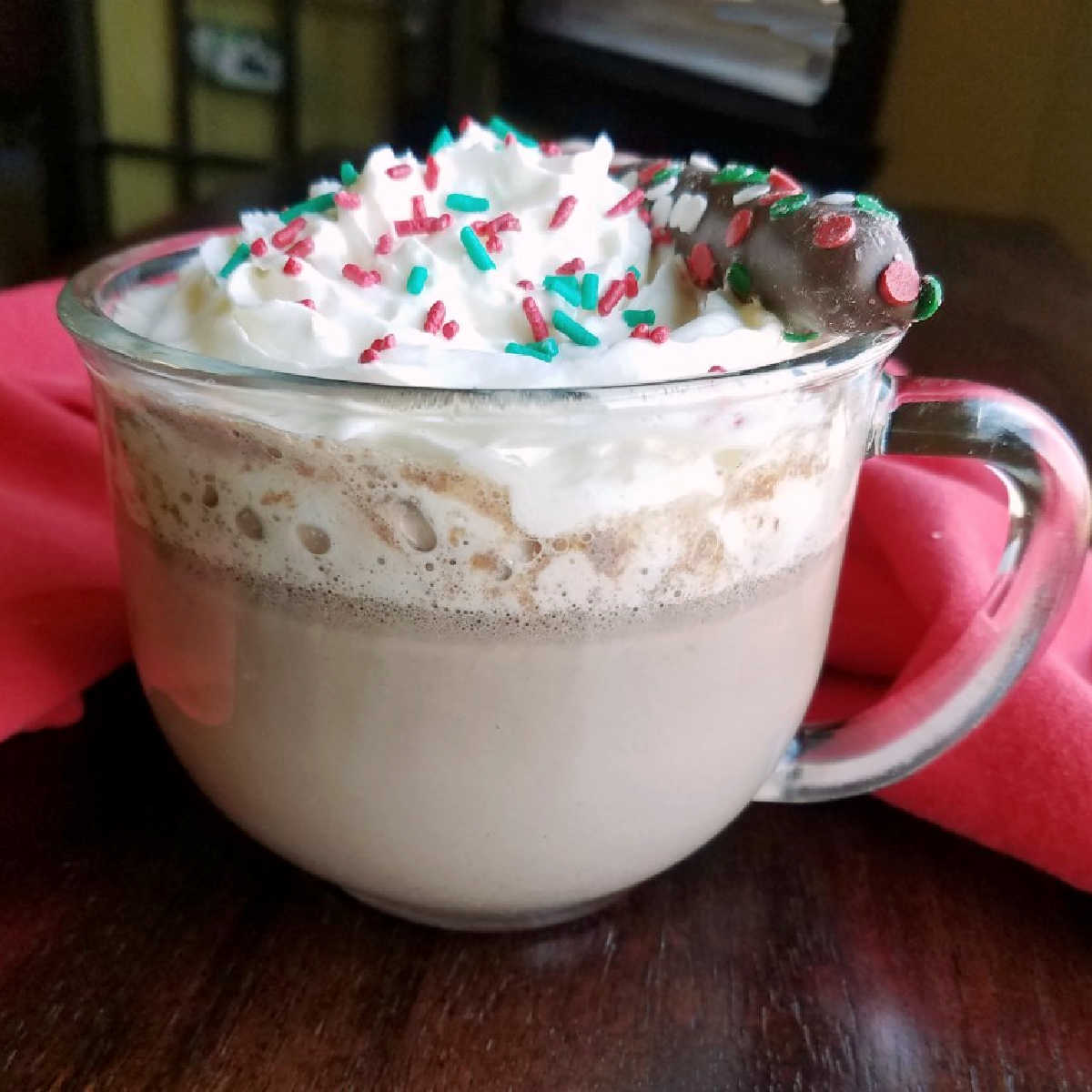 Large glass mug filled with creamy crock pot hot chocolate topped with whipped cream and sprinkles.