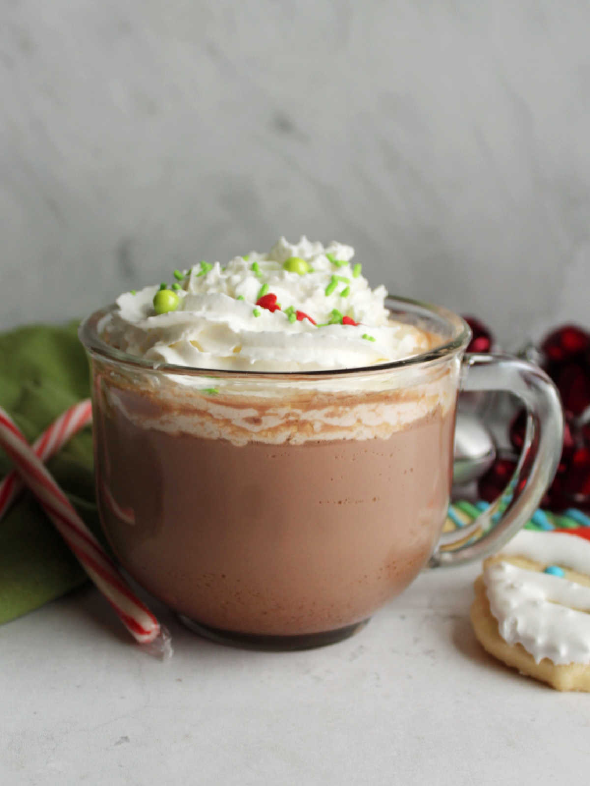 Mug of condensed milk hot chocolate topped with whipped cream served with a decorated sugar cookie and a couple of candy canes.