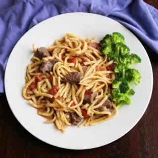 plateful of egg noodles cooked in beef and tomato mixture served with broccoli.
