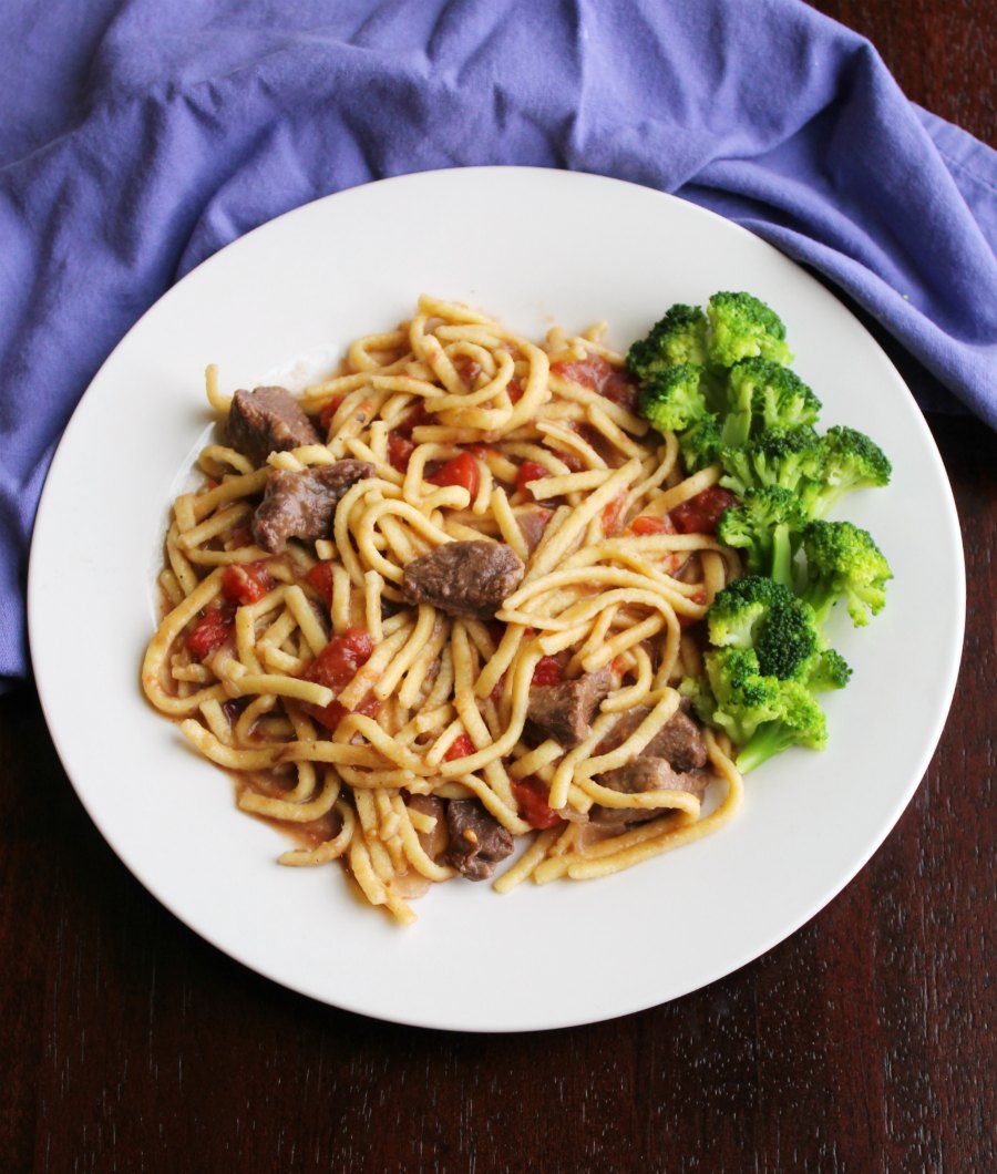 plateful of egg noodles cooked in beef and tomato mixture served with broccoli.