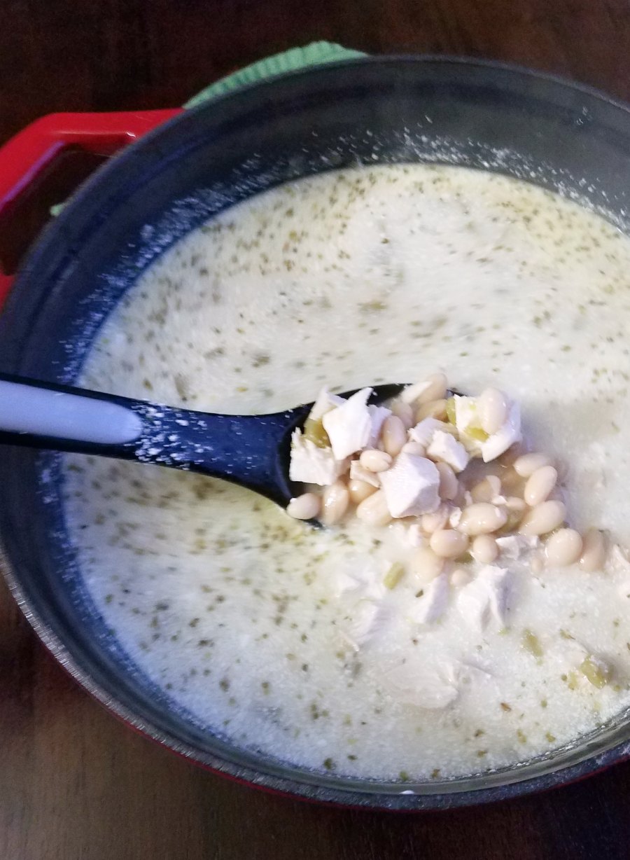 spoon lifting out a scoop of creamy white chicken chili with white beans and chunks of chicken and chilies.