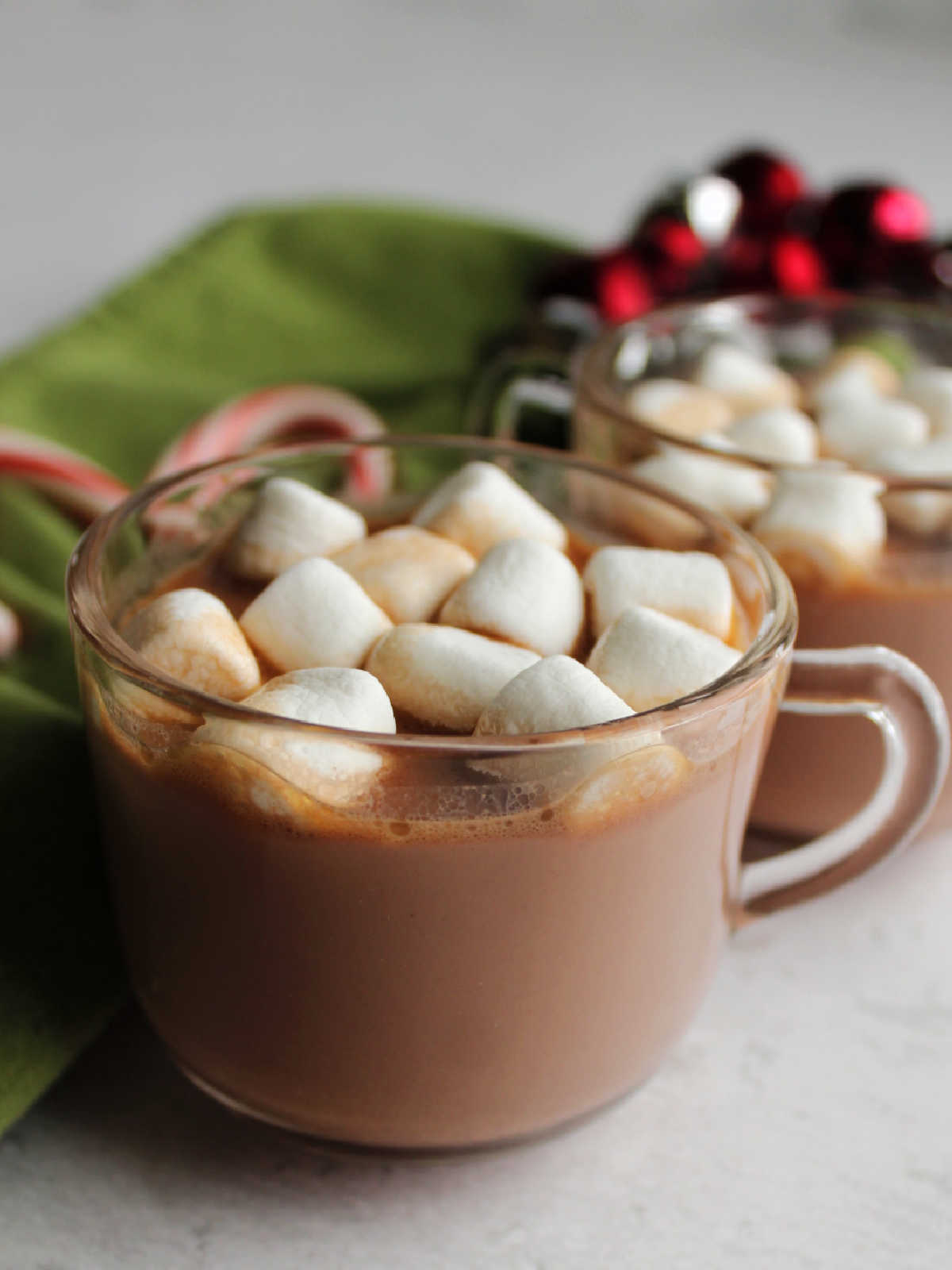 Small glass mugs with slow cooker hot chocolate topped with mini marshmallows and candy canes.