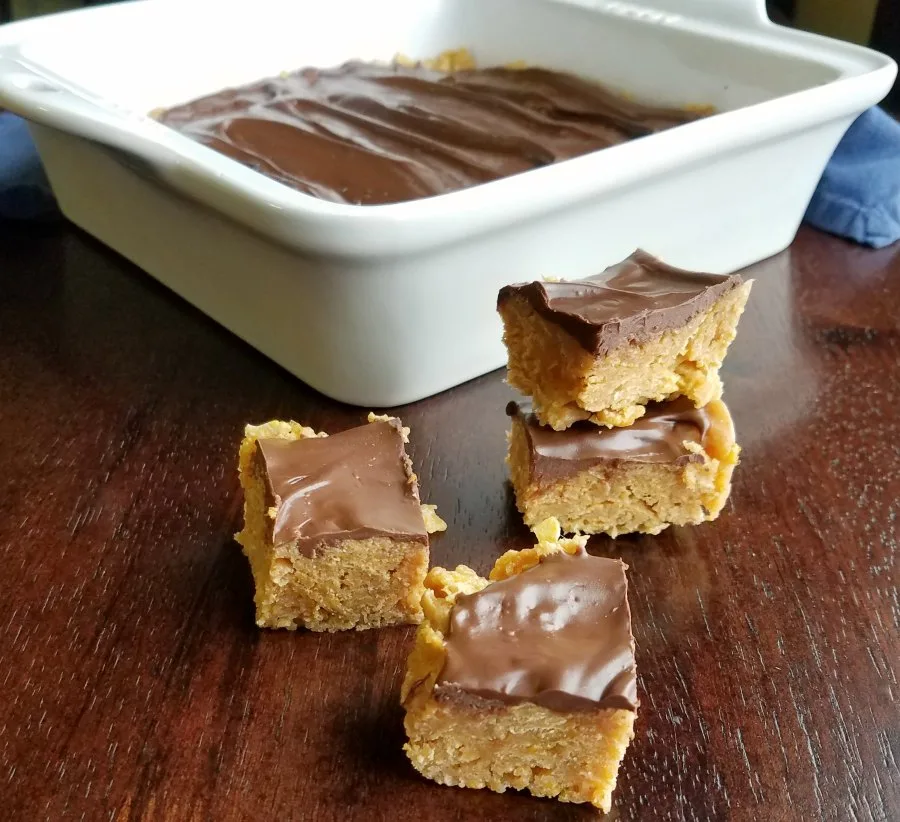 small squares of chocolate peanut butter corn flake bars in front of pan of treats