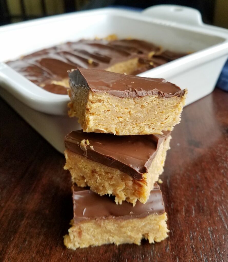large pieces of no bake chocolate peanut butter corn flake bars in front of pan of bars