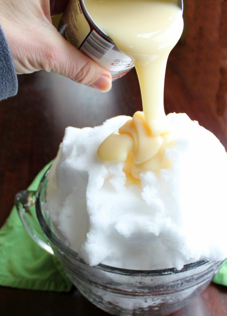 pouring can of sweetened condensed milk over bowl of snow