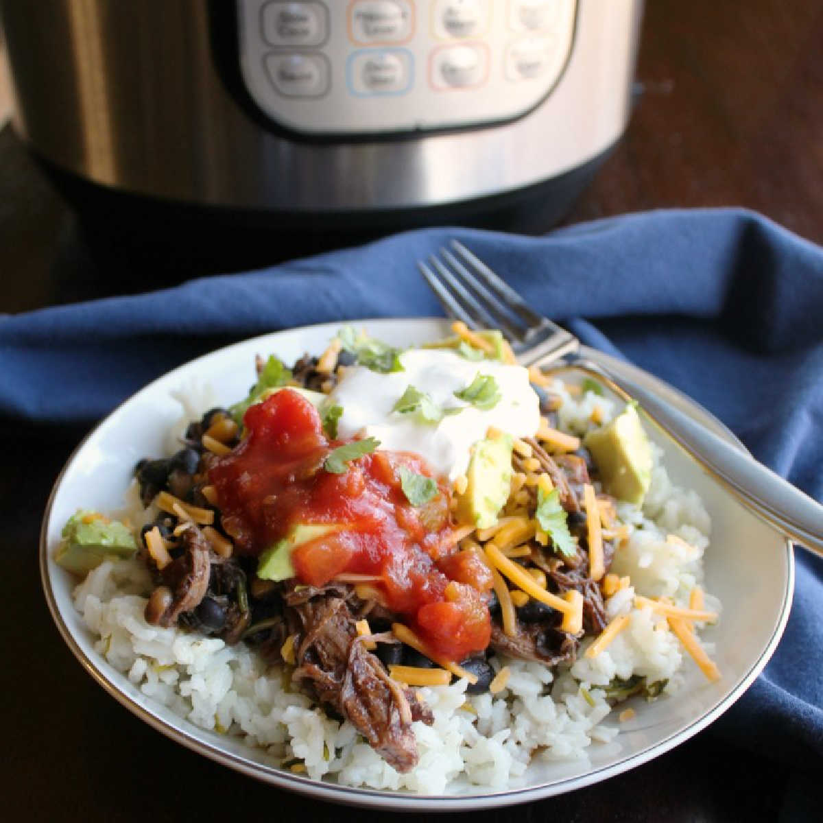 Burrito bowl made with cilantro lime rice, salsa chicken, salsa, sour cream, and shredded cheese in front of an instant pot.