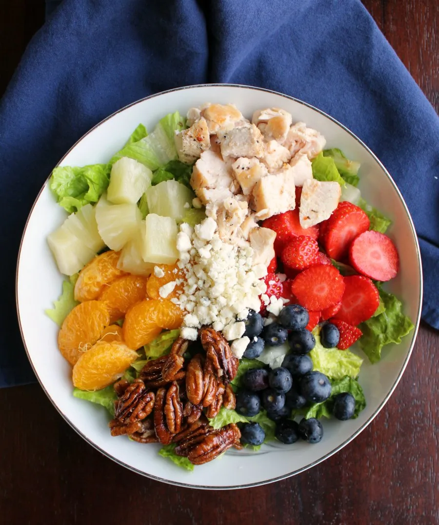 Salad topped with chunks of pineapple, mandarin oranges, strawberries, blueberries, chicken, pecans, and blue cheese served over lettuce.