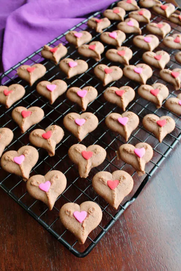 cooling rack full of chocolate spritz heart cookies with heart sprinkles.