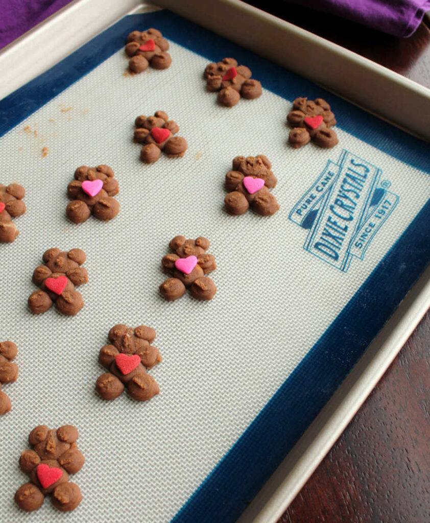 bear shaped chocolate spritz cookies with red and pink heart candies on top ready to be baked.