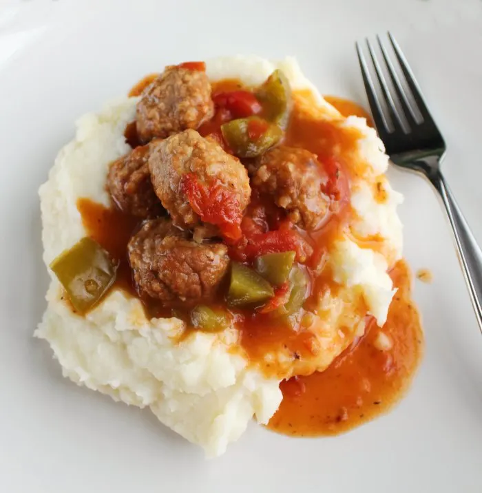 close pile of mashed potatoes topped with meatballs in tomato sauce with big pieces of bell pepper.