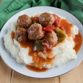plate full of mashed potatoes and swiss steak style meatballs with tomato gravy.