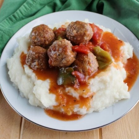 plate full of mashed potatoes and swiss steak style meatballs with tomato gravy.