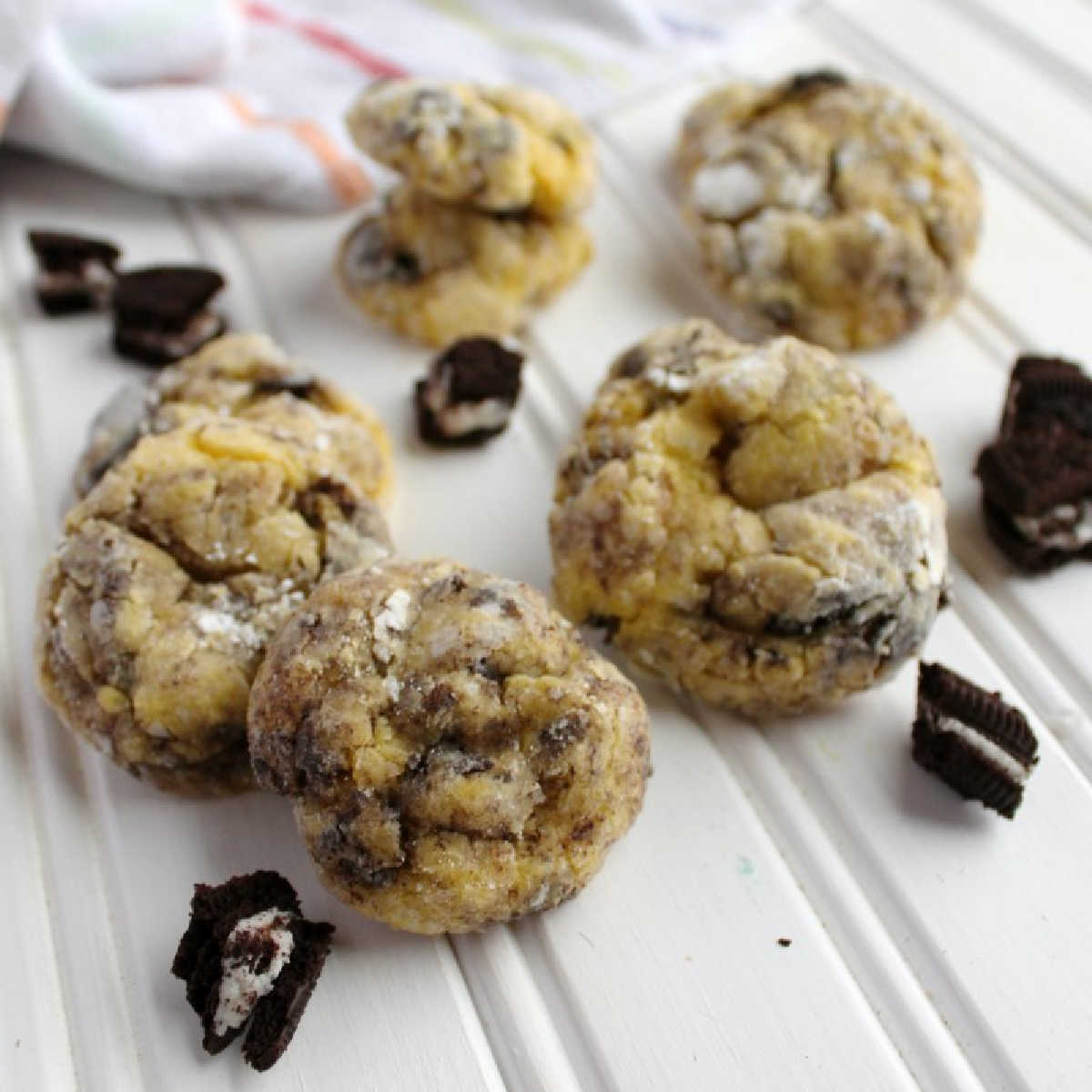 Soft cookies with bits of Oreos baked inside, coated in powdered sugar with more Oreo bits nearby.