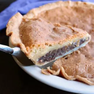 lifting first slice of toll house pie out of pan with gooey cookie like layer and lots of chocolate chips.