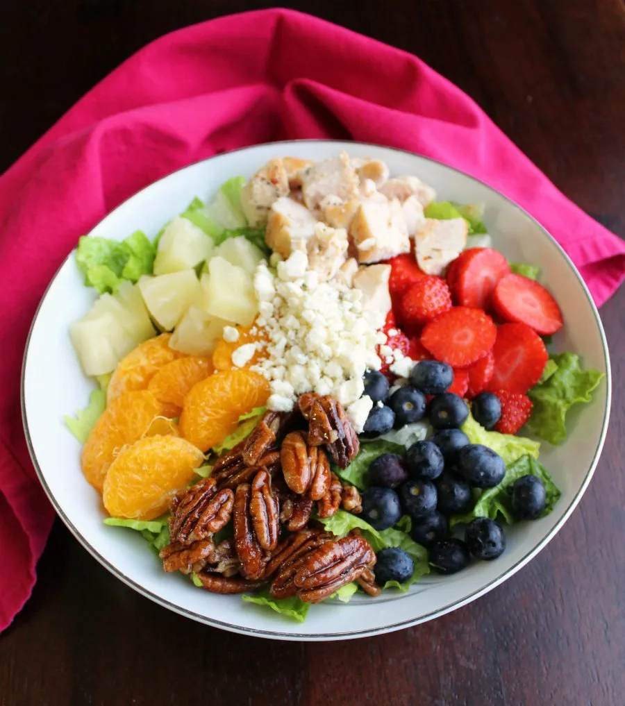 big bowl of salad greens topped with pineapple, orange sections, berries, chicken, pecans and cheese.