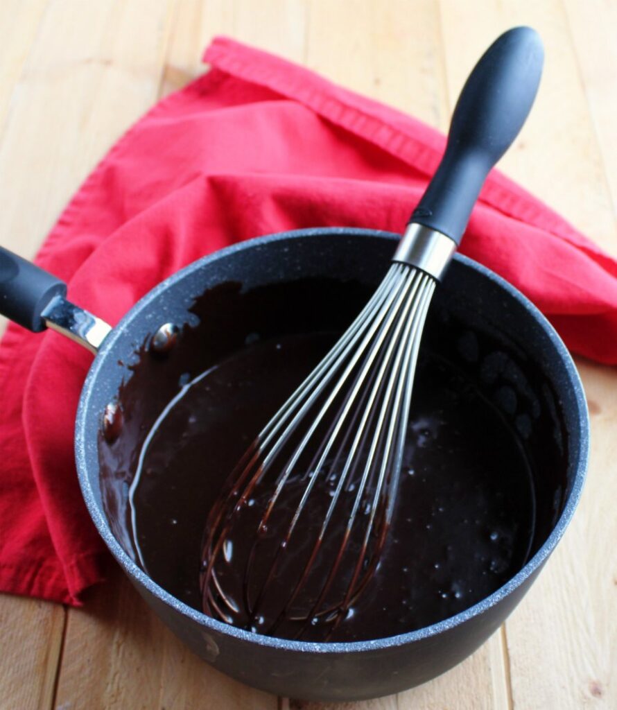 saucepan full of ganache style frosting and whisk.