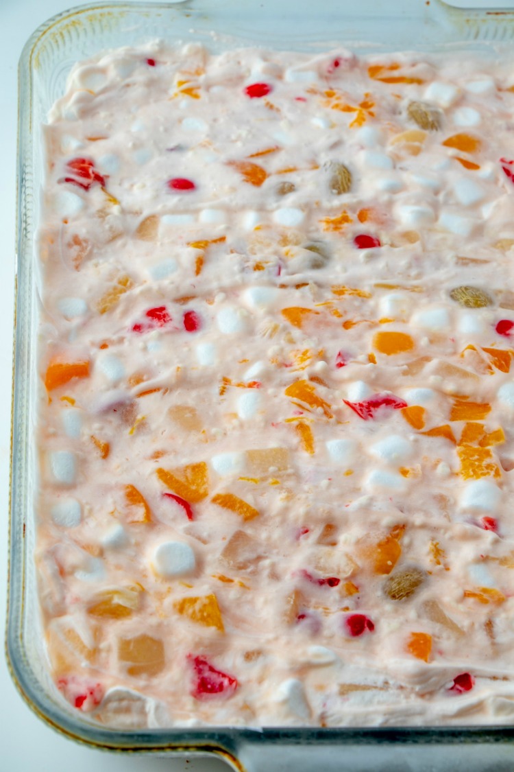 looking across a glass pan of frozen fruit salad with bits of fruit cocktail and marshmallows showing