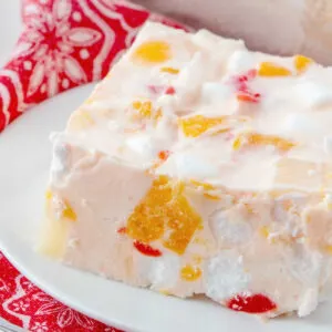 Close slice of frozen fruit salad showing fruit and marshmallows in peach frozen mixture.
