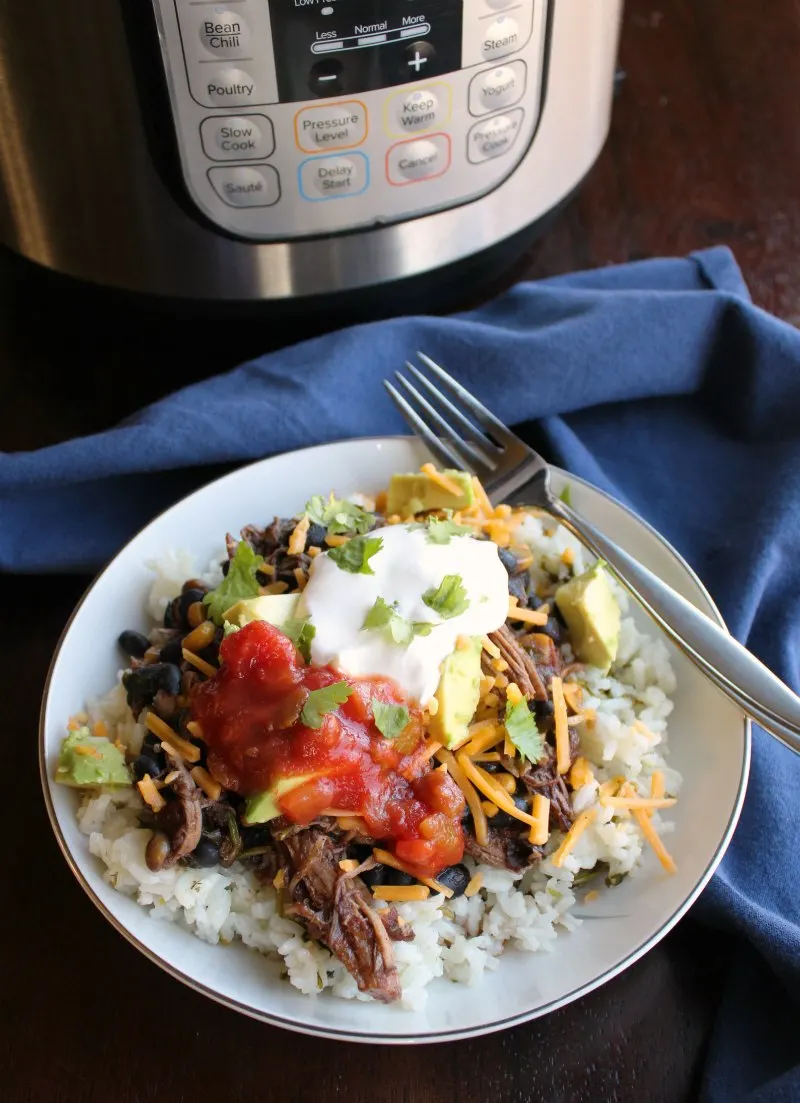 Rice bowl topped with salsa chicken, salsa, cheese, and sour cream in front of Instant Pot. 