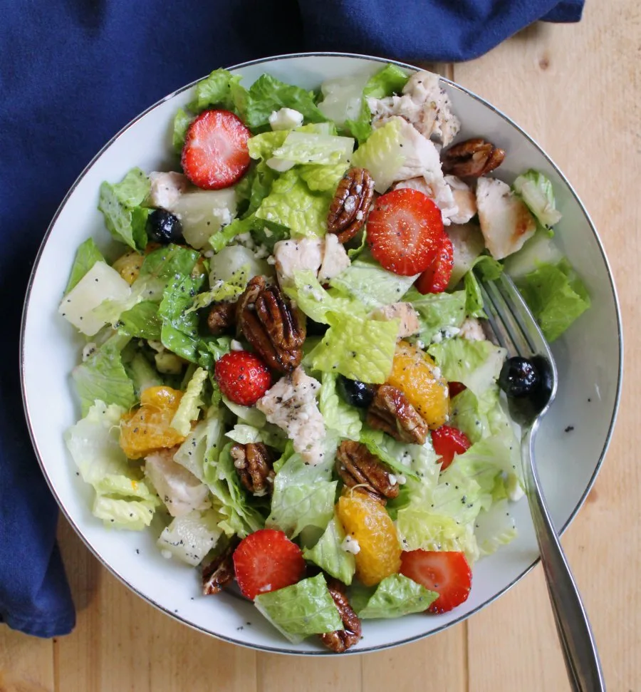 bowl of salad with romaine tossed with berries, oranges, pineapple, pecans, chicken and cheese.