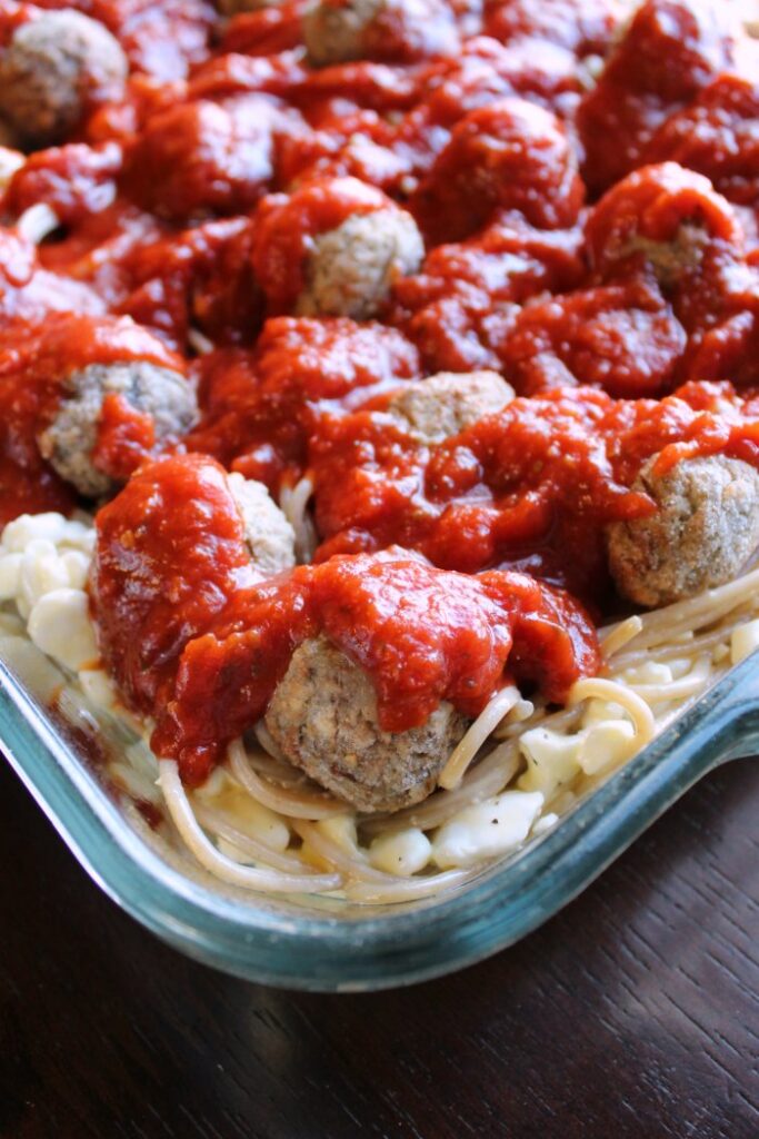 close up of corner of baking dish with creamy spaghetti mixture topped with meatballs and tomato sauce.