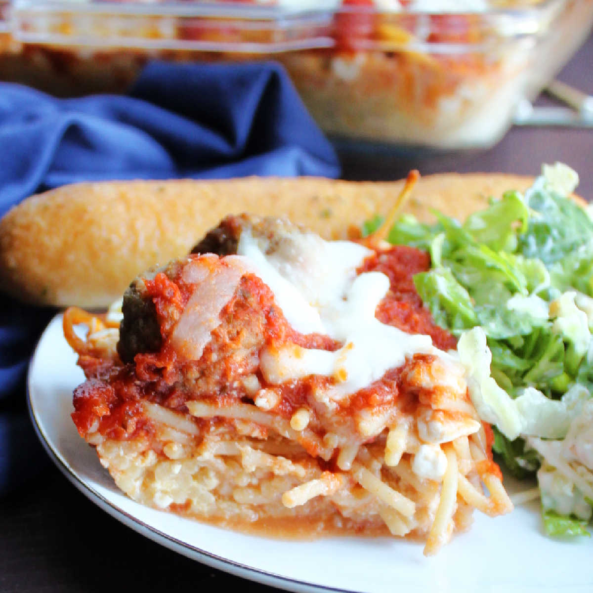 close up piece of spaghetti casserole with cheesy pasta layer topped with meatballs, tomato sauce and more cheese. 