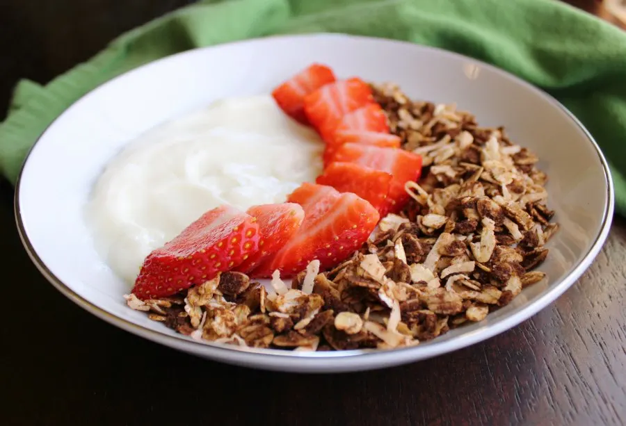 Bowl of vanilla yogurt with sliced strawberries and chocolate coconut granola.