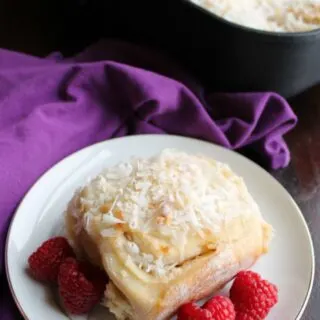 coconut sweet roll served with raspberries in front of pan of rolls