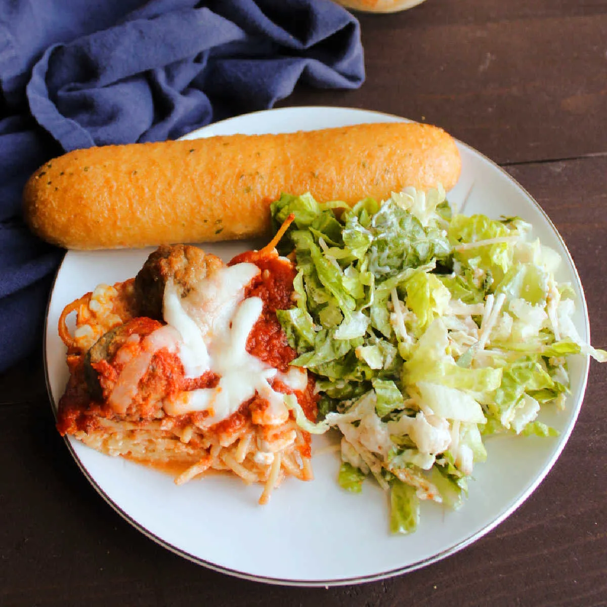 dinner plate filled with Caesar salad, breadstick and spaghetti and meatball bake.