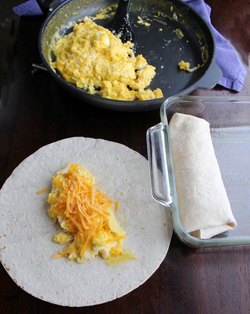 pan of scrambled eggs with some eggs and cheese on a tortilla ready to be rolled into burrito.