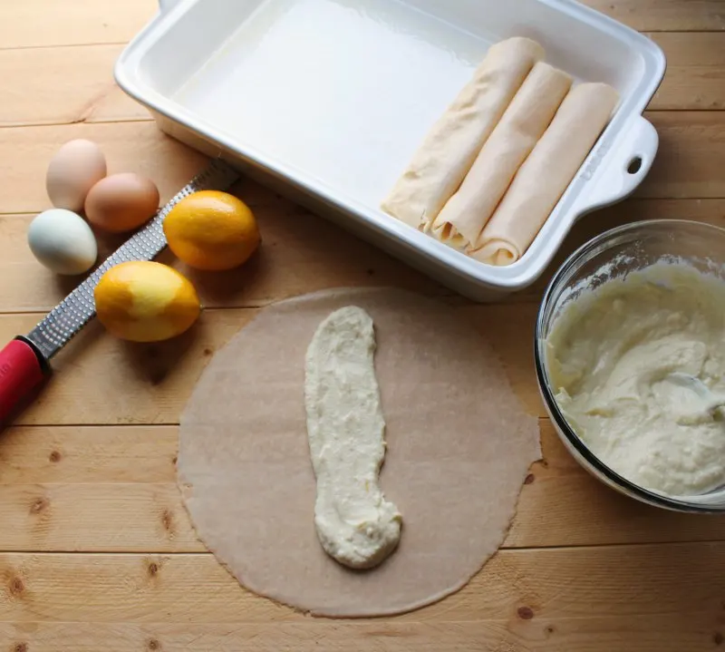 crepe being filled with lemon ricotta filling with zested lemon and eggs nearby.