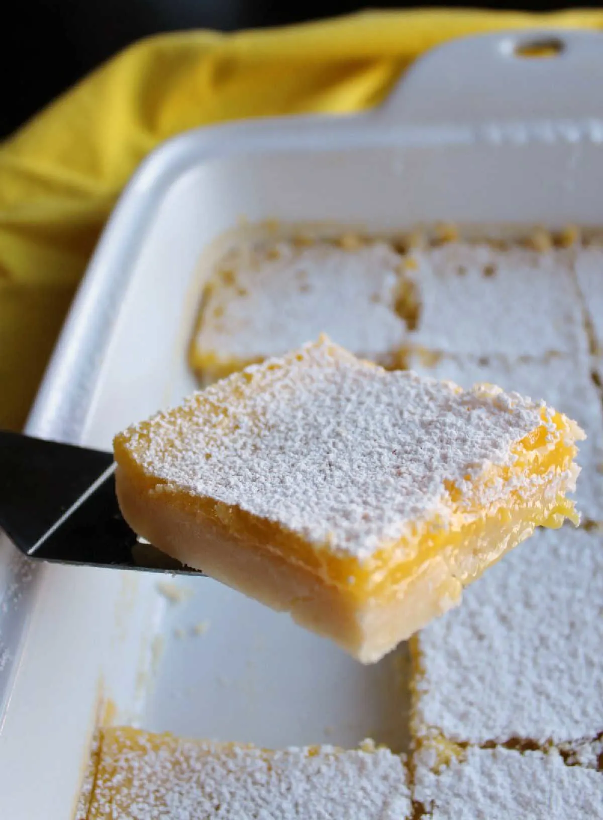 lifting piece of homemade lemon bars with shortbread crust and gooey lemon topping out of pan.