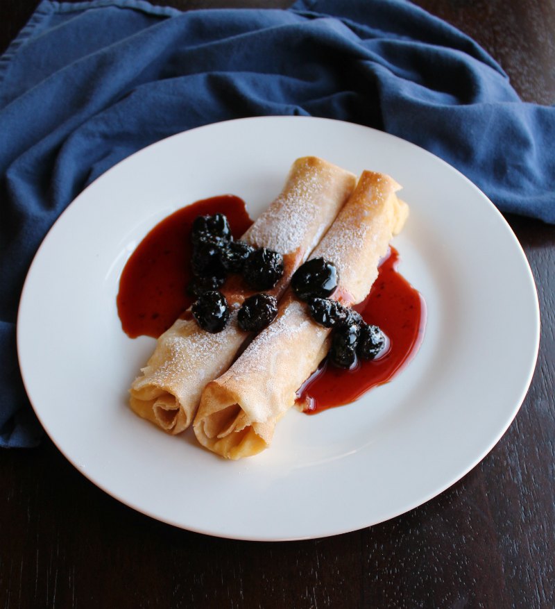 Place with two rolled crepes filled with lemon ricotta filling and topped with powdered sugar and cherry sauce.
