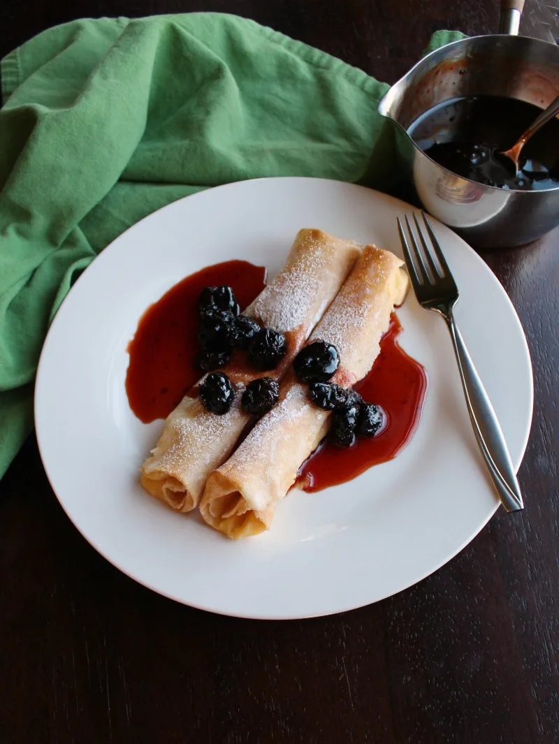 lemon ricotta stuffed crepes on plate with cherry syrup.