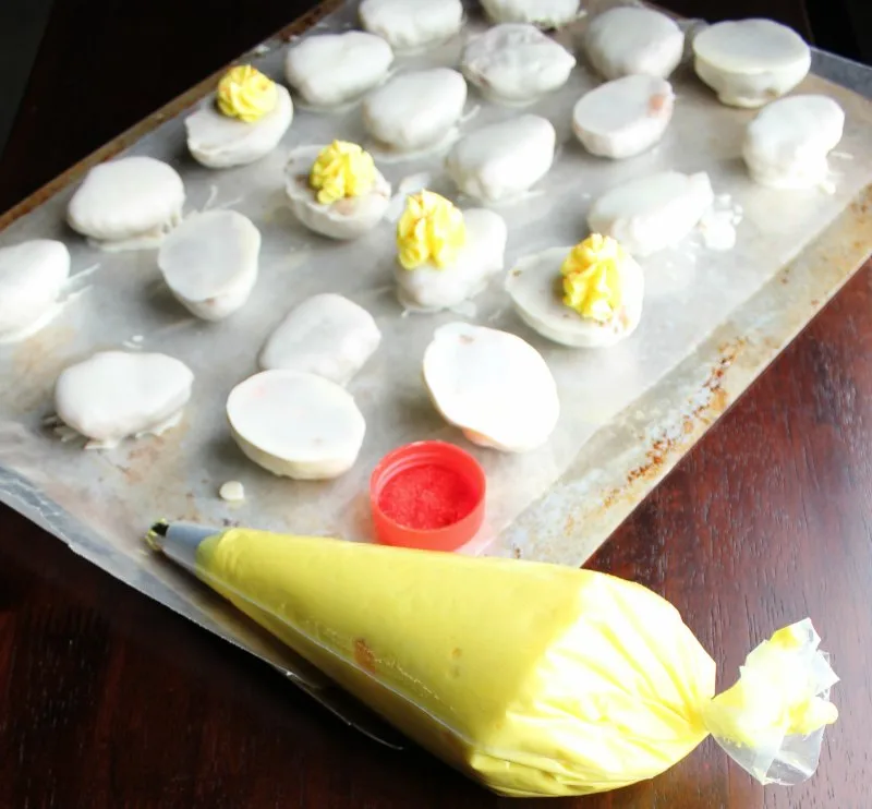 Egg shaped cake balls dipped win white chocolate with yellow frosting getting piped on for yolk filling.