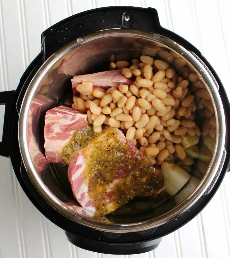chunks of pork, beans, onions and salsa verde in instant pot ready to cook.