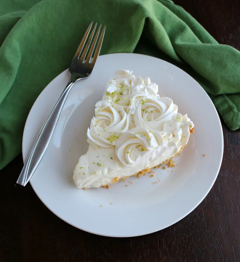 slice of key lime pie with whipped cream rosettes piped on it on plate with fork