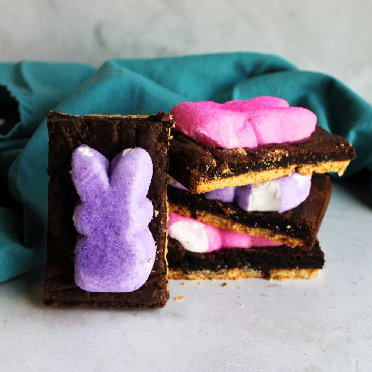Stack of Peeps smores bars showing graham cracker base, gooey brownie-like chocolate layer and melted bunny shaped peeps on top.