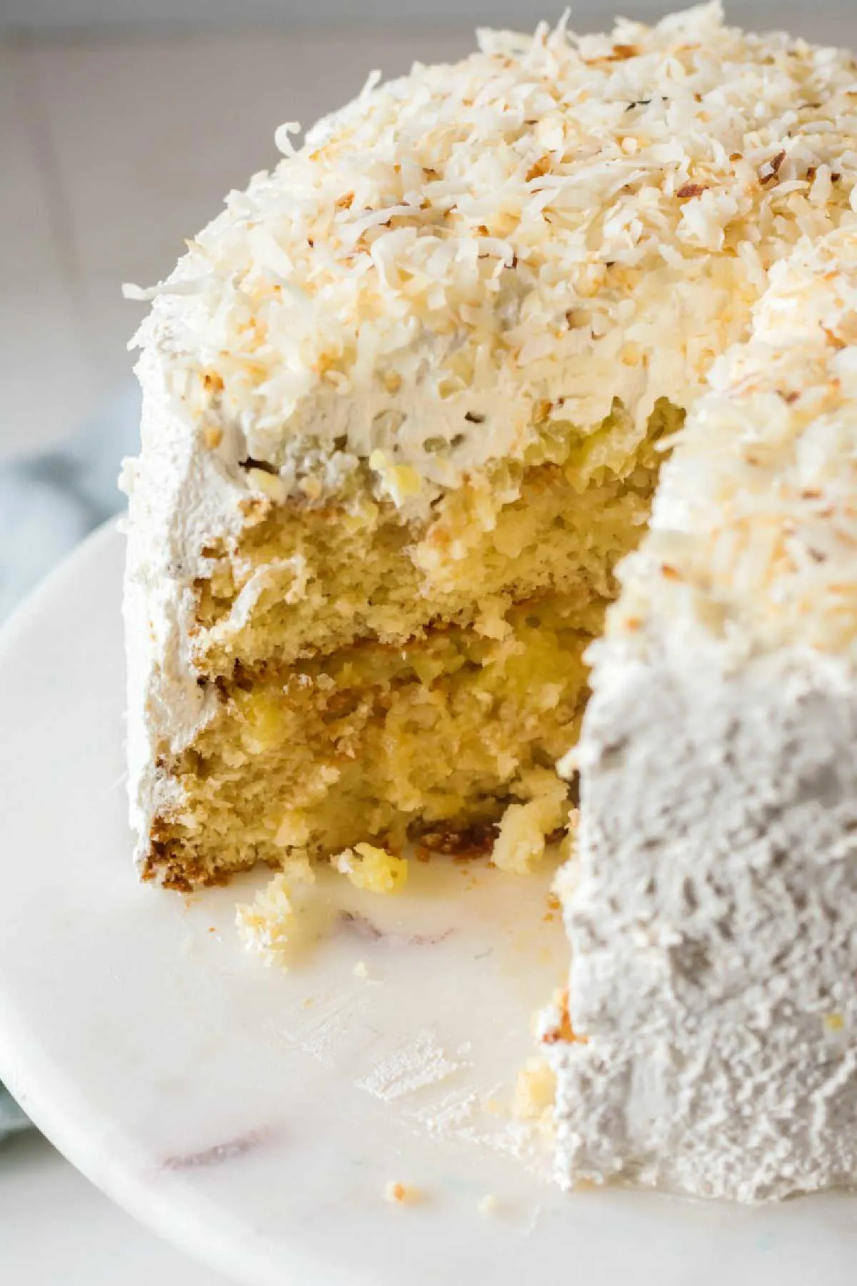 Inside of haleakala cake showing white cake, pineapple filling, fluffy white frosting and toasted coconut.