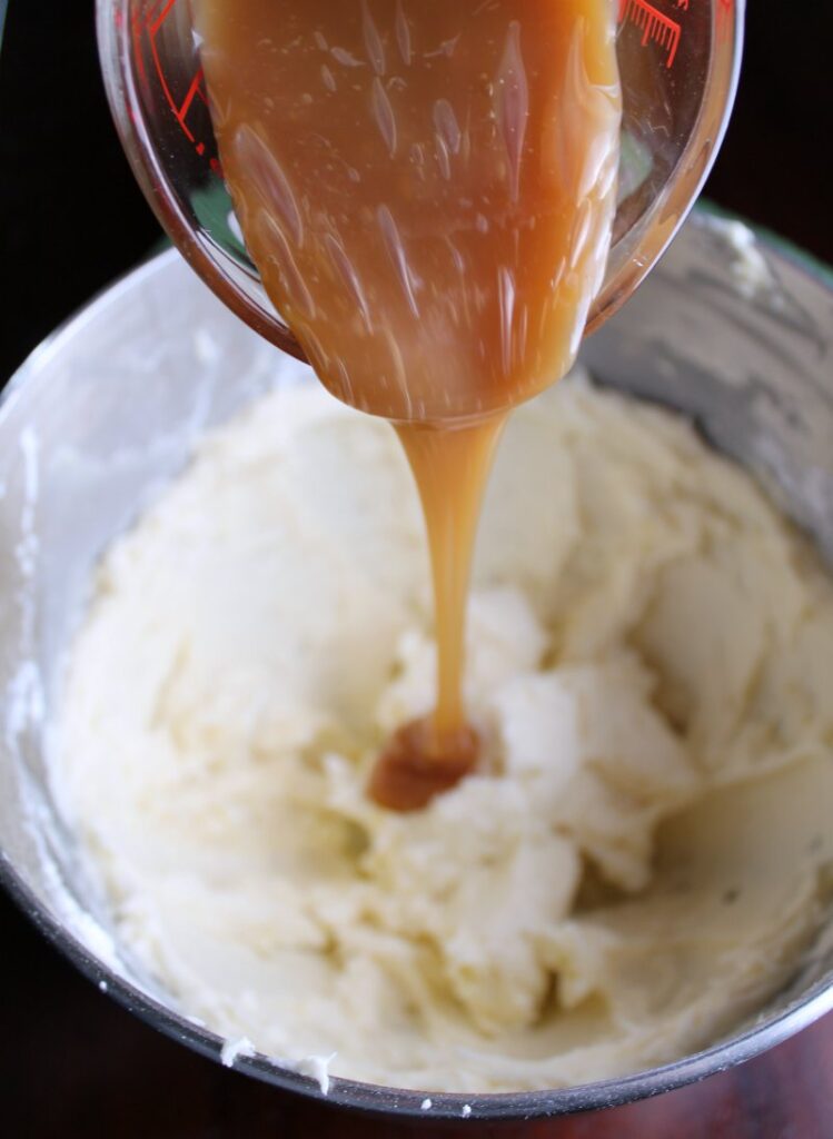 pouring caramel into mixing bowl full of buttercream