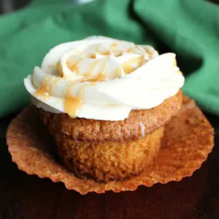 carrot cake cupcake with wrapper pulled down, caramel frosting on top and drips of caramel topping.