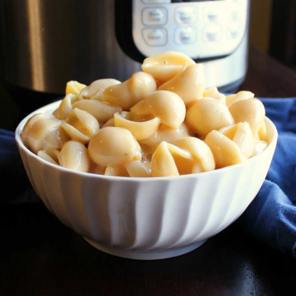 close up bowl of creamy shells and cheese in front of instant pot.