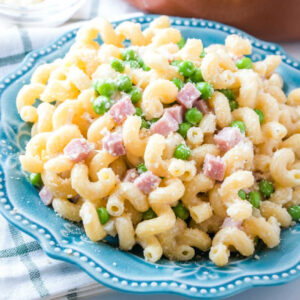 Close up plate of curly pasta with cubes of ham, peas and paremsan cheese.