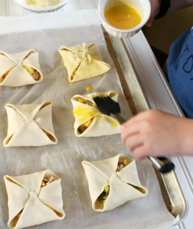 Little Dude brushing hand pies with egg yolk wash and topping with cheese.