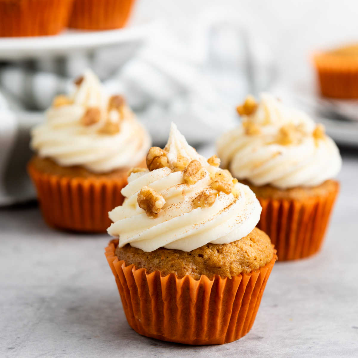 Carrot cake cupcakes in orange paper liners and topped with piped frosting and chopped walnuts.