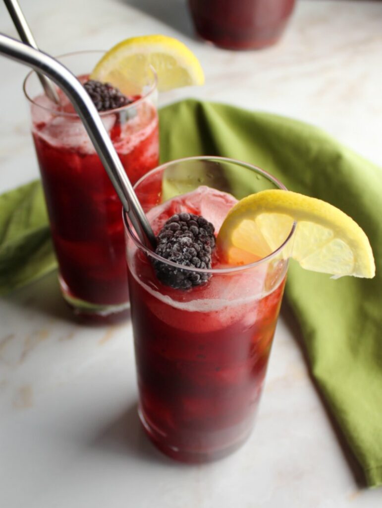 Lokking down on a couple of glasses of deep purple blackberry lemonade with berries and lemon wedges with stainless steel straws, ready to drink. 