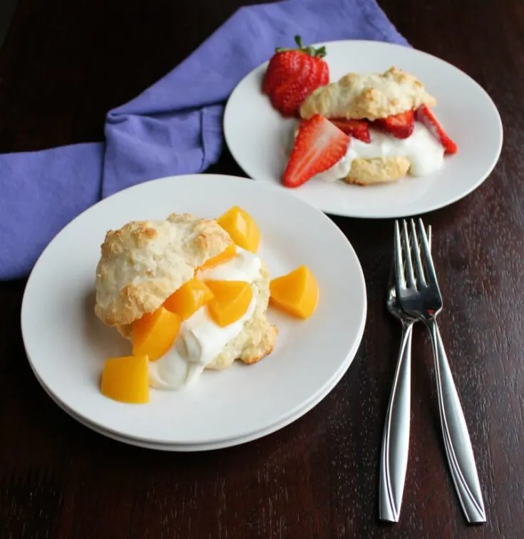 two plates, one with a peach brunch shortcake and one with sliced strawberries and yogurt in a biscuit.